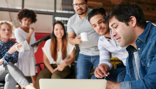 Group of coworkers huddled around a laptop screen while one explains a concept