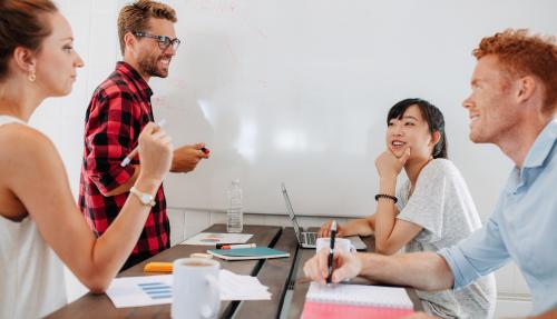 Group of coworkers chatting around a table and using whiteboard