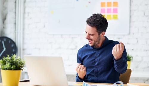 Male celebrating by fist pumping whilst looking at laptop