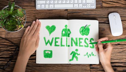 Two hands illustrating wellness and factors that contribute on a notepad