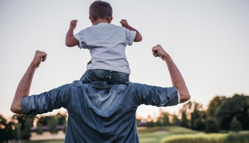 Child sitting on male's neck, both child and adult are raising their arms